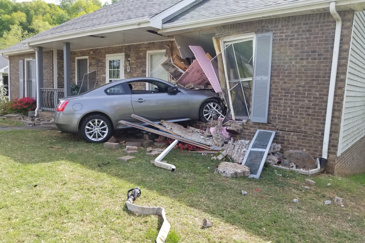 Photo showing a car that drove into someone's home. Debris is sprawled all over the yard